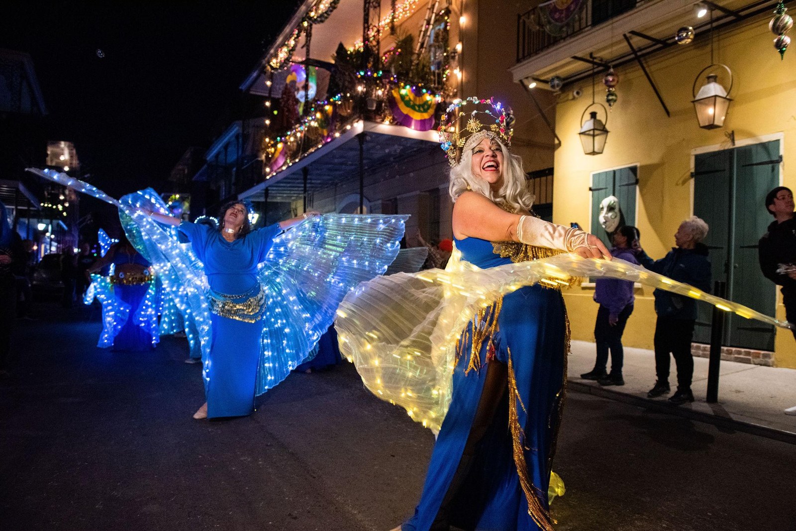 Dancers spreading illuminated blue and gold wings on a nighttime street