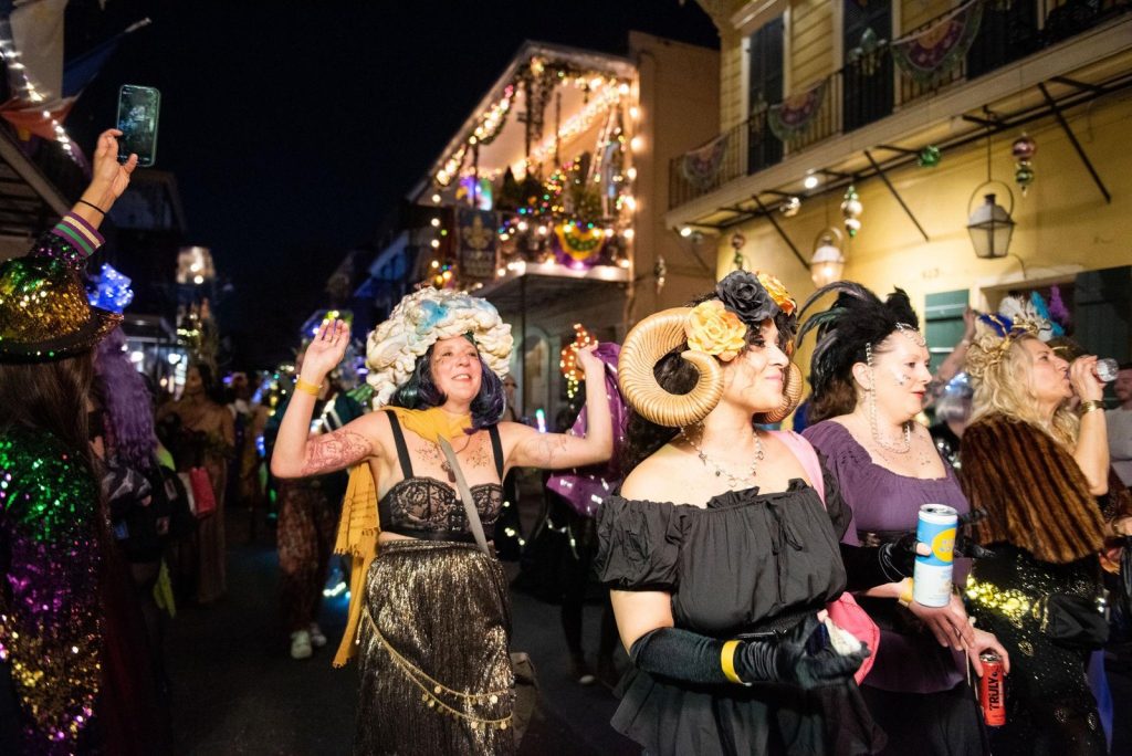Revelers wearing animal horns and feathers joyously raise their hands to pump up the crowd as they parade down the street.